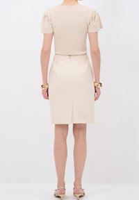 Vestido ajustado beige con mangas cortas abullonadas y cremallera trasera, que cuenta con una textura suave y una falda lápiz a la altura de la rodilla con una abertura trasera.