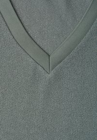 Gros plan d'un tissu tricoté gris-vert texturé avec un col ou un détail d'encolure côtelée en forme de V.