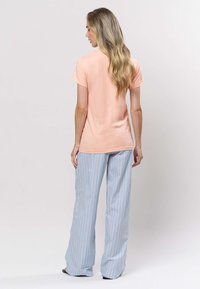 Persikanvärinen T-paita, jossa on lyhyet hihat ja pyöreä pääntie, yhdistetty vaaleansinisiin raidallisiin leveälahkeisiin housuihin. Sileä kangas ja rento istuvuus.