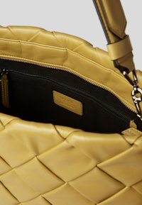 Yellow woven leather handbag with black fabric interior, zipped pocket, and matching leather label inside.