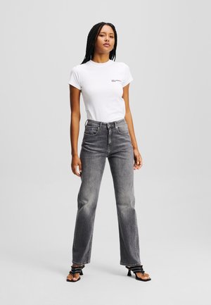 T-shirt bianco attillato con un piccolo logo, abbinato a jeans grigi a vita alta. I jeans hanno una gamba dritta e dettagli classici delle tasche.