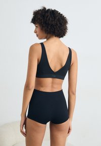 Schwarzer Sport-BH mit breiten Trägern und V-Rückendesign, kombiniert mit hoch taillierten schwarzen Shorts, beide aus weichem, dehnbarem Material gefertigt.
