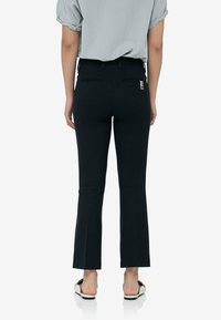 Czarne spodnie w kształcie dzwonów z średnim stanem, gładką teksturą, tylnymi kieszeniami i zamkiem błyskawicznym, połączone z szarą bluzką.