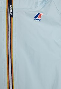 Giacca a vento di colore azzurro chiaro con una superficie liscia, caratterizzata da una zip centrale con strisce multicolori e un logo K-Way.