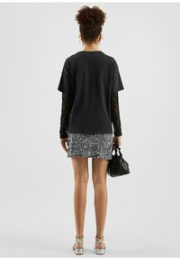 Zwarte oversized t-shirt gelaagd over een lange mouwen kanttop, gecombineerd met een glanzende zilveren pailletten minirok en metallic sandalen met bandjes.