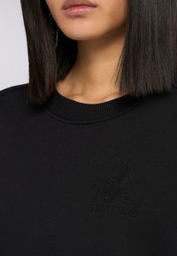 Czarna bluza z ribbowanym dekoltem i wytłoczonym logo Trussardi z wzorem wyżła, wykonana z teksturowanej tkaniny.