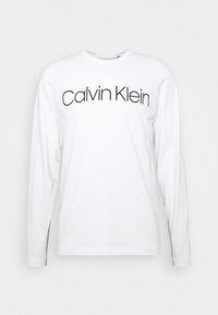 Long-sleeve white cotton t-shirt featuring a black "Calvin Klein" logo centered across the chest, with a crew neckline and standard fit.
