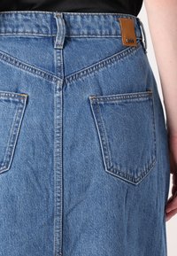 Gonna di denim di colore azzurro chiaro con vita alta, due tasche posteriori e una patch in pelle color tan. Presenta cuciture in vista e un design dritto.