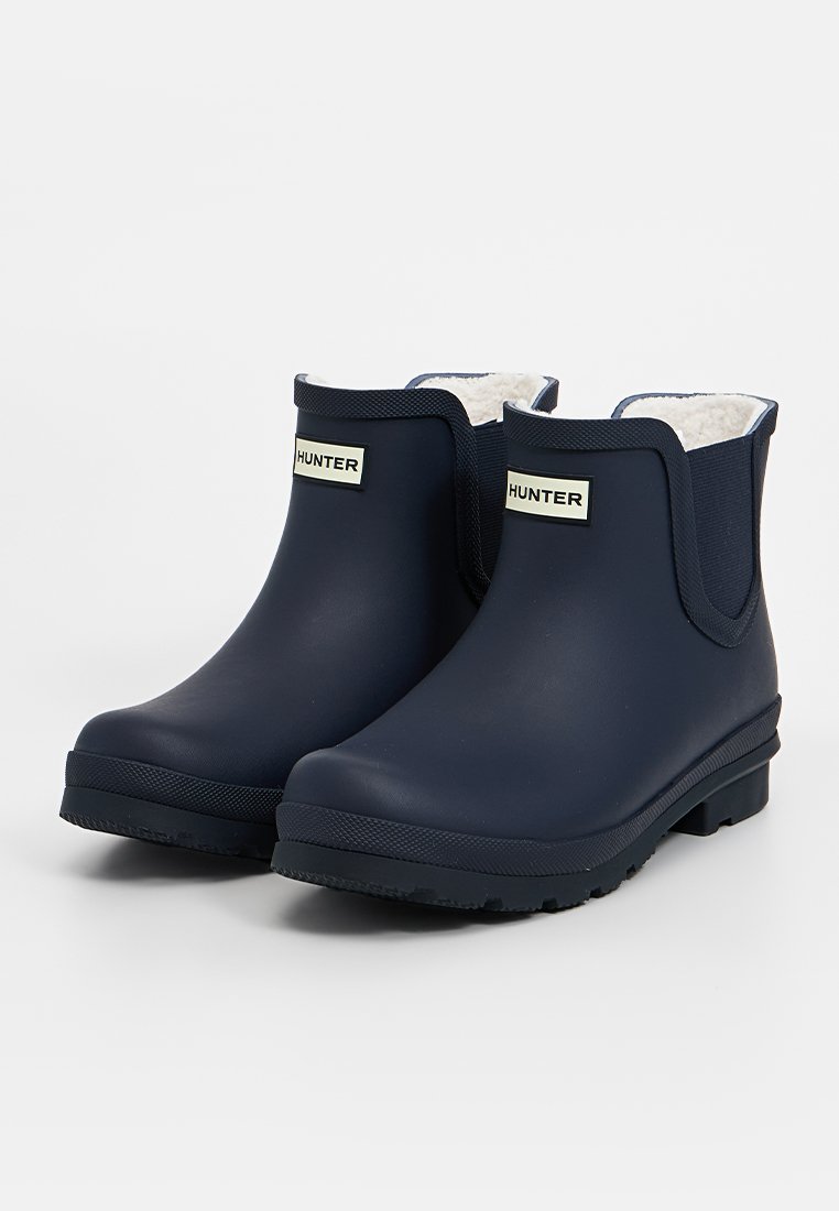 Bottes de mer en caoutchouc, avec une texture lisse, des panneaux latéraux élastiques, une doublure en fausse fourrure blanche et une semelle en caoutchouc noire, arborant le logo "HUNTER".
