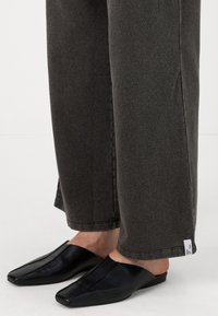 Sive jeans širokih nogavic z božnim označevalcem in črnimi usnjenimi natikači z zašiljenim nosom in gladko teksturo.