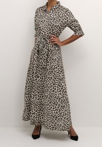 Maxikleid mit Leopardenmuster, Kragen, kurzen Ärmeln, Gurt in der Taille und leichtem Stoff, der schwarze und hellbraune Flecken auf einem cremefarbenen Hintergrund zeigt.