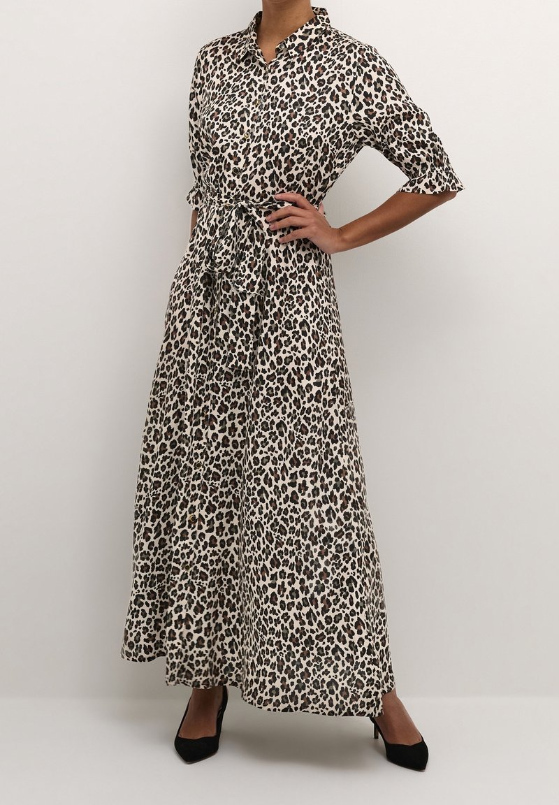 Maxikleid mit Leopardenmuster, Kragen, kurzen Ärmeln, Gurt in der Taille und leichtem Stoff, der schwarze und hellbraune Flecken auf einem cremefarbenen Hintergrund zeigt.