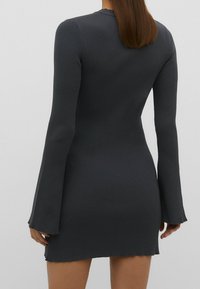 Vestido mini de canalé, elástico y gris oscuro que cuenta con mangas largas acampanadas y cortes laterales para facilitar el movimiento. Sencillo escote redondo.