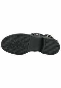 Suela de zapato negra con goma texturizada. Presenta patrones de agarre elevados y un logo en relieve. Incluye un talón ligeramente elevado y forma redondeada.