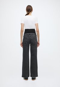 Μαύρο τζιν με πλατύ πόδι και ψηλή μέση, υφασμένο από υφή ντένιμ, με διακριτικές πίσω τσέπες. Συνδυασμένο με ένα εφαρμοστό λευκό t-shirt.