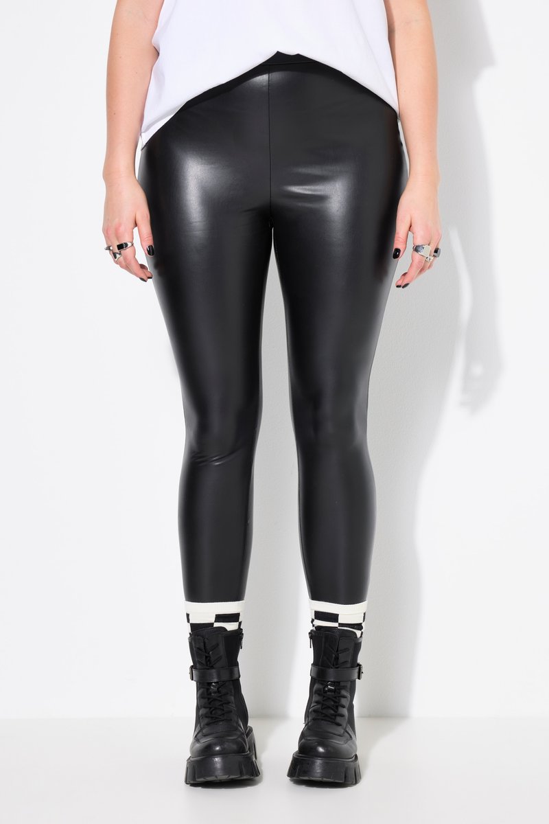 Person trägt glänzende schwarze Lederleggings, schwarze Kampfstiefel, weiß-schwarz gestreifte Socken und ein weißes ärmelloses Top.