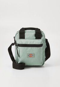 Mintgrön canvas crossbody-väska med svarta remmar, utrustad med en framficka med dragkedja och en logotypmärke. Kompakt och rektangulär design.