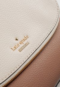Beige and brown leather handbag with a textured finish, gold hardware, and a visible logo detail, featuring a zipper closure.