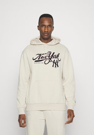 Sudadera beige con un bolsillo tipo canguro en la parte delantera, capucha con cordón y logo impreso de "NewYork" en negro y rojo oscuro, puños y dobladillo de canalé.