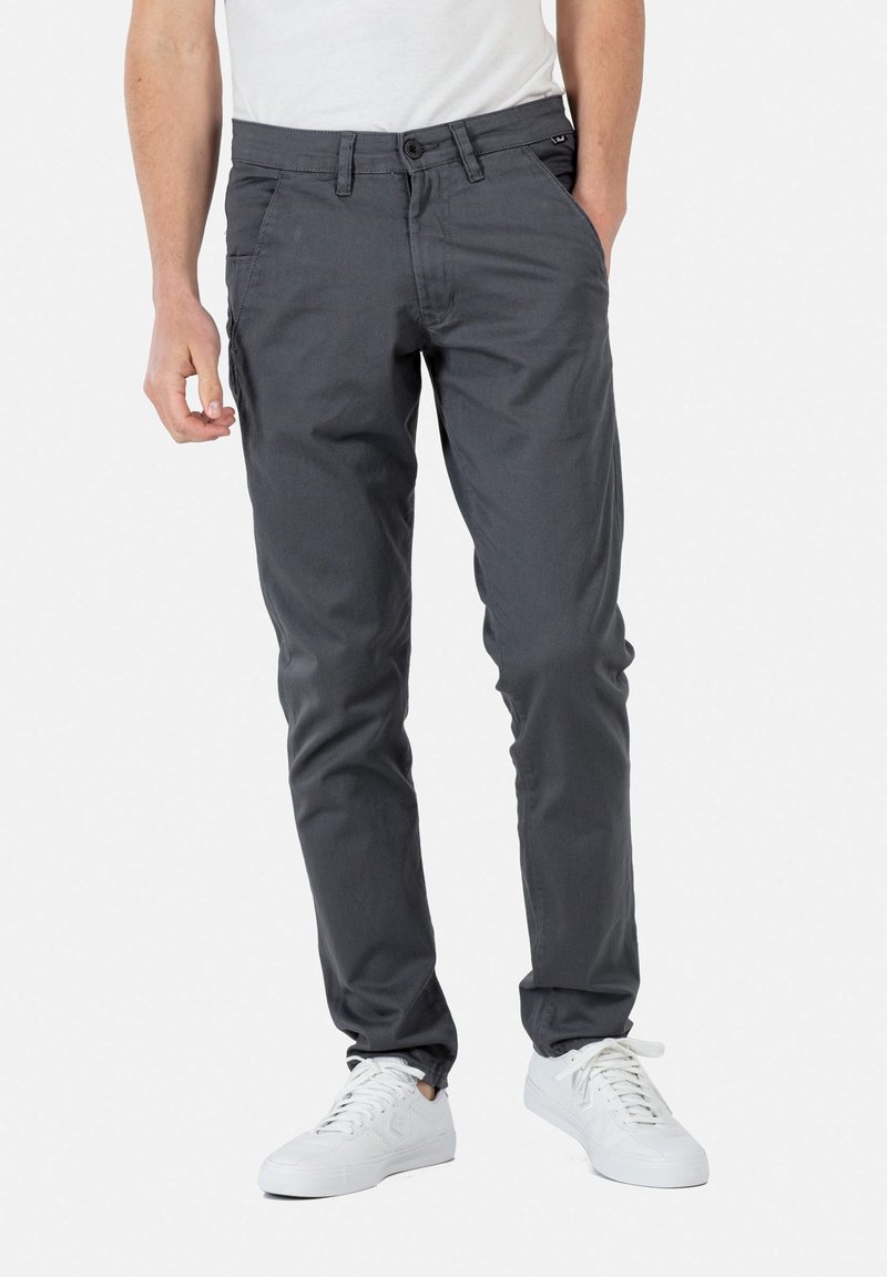 Pantalones de mezcla de algodón grises con corte slim, bolsillos frontales, cierre de botón y acento de logo cerca de la cintura. Llevados con zapatillas blancas.