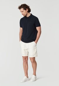 Marinblå polo t-shirt med kort ärm, i kombination med vita linneshorts och vita sneakers. T-shirten har en diskret logodetalj.