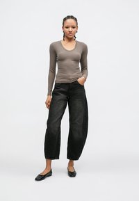 Top s dlouhými rukávy a výstřihem do oblouku v světle hnědé žebrované látce, kombinovaný s černými širokými kalhotami s vysokým pasem a černými nízkými botami.