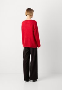 Rød, oversized genser med en myk tekstur, vide ermer og rund halslinning, kombinert med svarte vide bukser og høyhælte sko.
