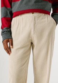 Beige korduroja bikses ar vertikālām ribām, ar pogu aizdari jostasvieta, sānu kabatām un brīvu piegriezumu.