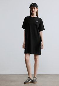 Čierne tričkošaty s krátkymi rukávmi a bočnými rozparkami, s malým bielym logom. Kombinované s čiernou šiltovkou a sivými teniskami.