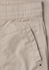 Pantalon beige avec ceinture élastique, poche avant en biais et détails de couture visibles sur tissu lisse.