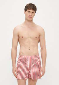 Shorts de bain à rayures rouges et blanches avec une taille élastique, offrant une coupe décontractée et un design simple. La texture semble lisse.