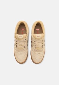 Beige Wildleder- und Mesh-Sneaker mit Gummisohle, Schnürdesign und subtilen braunen Streifen. Markenlogo auf der Zunge und an der Seite.