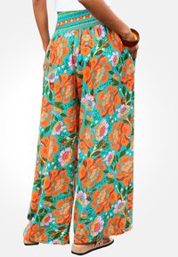 Pantaloni a palazzo floreali con vita smock, caratterizzati da fiori arancioni e rosa su uno sfondo turchese. Include tasche laterali.