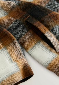 Woolen fabric featuring a houndstooth pattern in brown, black, and white, with visible stitching and a soft, textured surface.