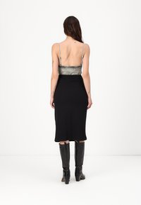 Black midi dress with sleek, fitted design, featuring a metallic silver bodice and thin straps, paired with glossy black knee-high boots.