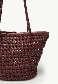 Flätad vinröd tote-väska med vävd textur, med två flätade handtag och ett litet guldemblem på sidan.