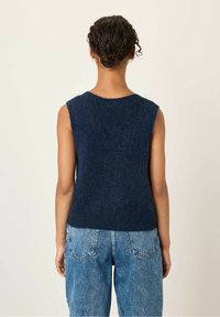Marineblauwe mouwloze gebreide trui met een zachte, gestructureerde afwerking, voorzien van een ronde halslijn en een iets cropped zoom, gecombineerd met high-waisted jeans.