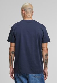 Tricou din bumbac de culoare bleumarin, cu mâneci scurte și decolteu rotund. Textură netedă, design simplu, fără modele sau accente vizibile.
