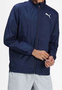 Navy blue lightweight jacket with a zip closure, elastic cuffs, and a white Puma logo on the chest. Smooth texture and casual design.