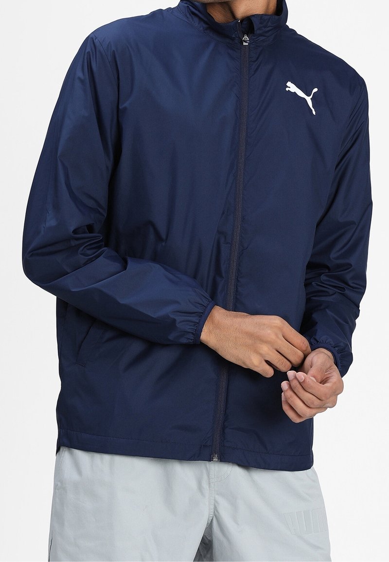 Navy blue lightweight jacket with a zip closure, elastic cuffs, and a white Puma logo on the chest. Smooth texture and casual design.