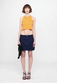 Oranžs ribots kroptops, tumši džinsa svārki ar divām priekšējām kabatām, melnas strappy sandales un teksturēta melna soma.