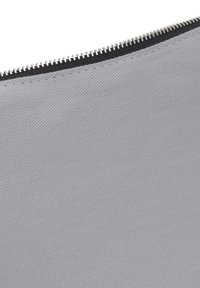 Material de tela gris con una textura diagonal, que cuenta con una cremallera negra. La tela tiene un acabado suave y una costura sutil a lo largo de los bordes.