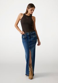 Denim maxi skirt with a side slit, featuring a fitted silhouette, light blue color, two front pockets, and embroidered accents.