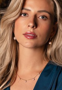 Collier en or avec de petites perles, porté avec des boucles d'oreilles pendantes assorties en perles. Le collier présente des maillons de chaîne délicats et un design simple.