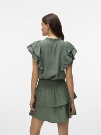 Robe verte à plusieurs couches avec des manches volantées, taille smockée et détail en trou de serrure à l'arrière. Fabriquée en tissu léger et texturé.