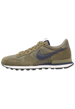 Niedriger olivgrüner Sneaker mit navyblauem Nike-Swoosh, Schnürdesign, Obermaterial aus Wildleder und Mesh sowie weißer und navyblauer Sohle.