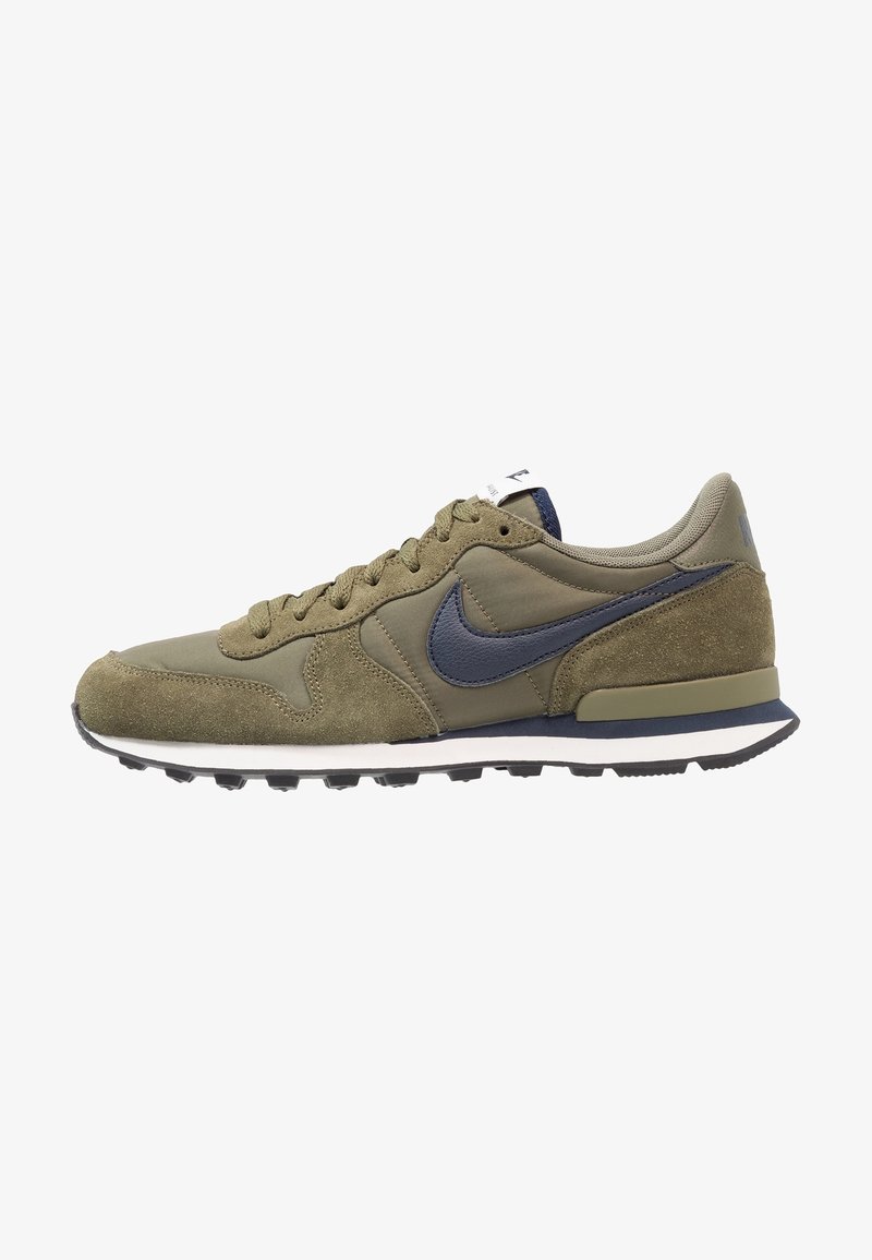 Baskets basses vert olive avec le swoosh Nike bleu marine, design à lacets, dessus en daim et mesh, et semelle blanche et bleu marine.