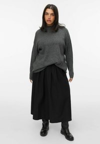 Grijze oversized trui met een hoge halslijn in combinatie met een zwarte geplisseerde rok en kniehoge zwarte laarzen. Eenvoudig en minimalistisch ontwerp.