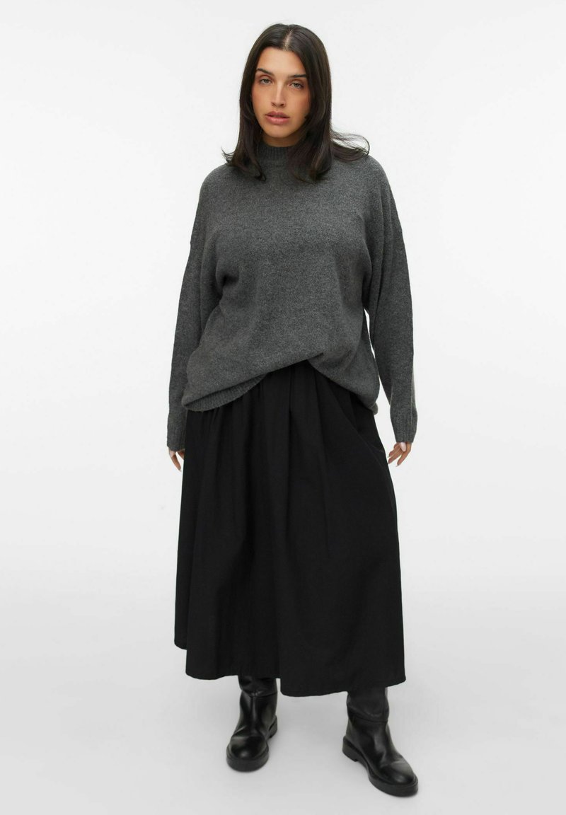 Grijze oversized trui met een hoge halslijn in combinatie met een zwarte geplisseerde rok en kniehoge zwarte laarzen. Eenvoudig en minimalistisch ontwerp.