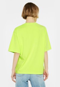 Neon-grünes Baumwoll-T-Shirt mit lockerer Passform, kurzen Ärmeln und Rundhalsausschnitt. Schlichte Rückseite ohne zusätzliche Muster oder Details.